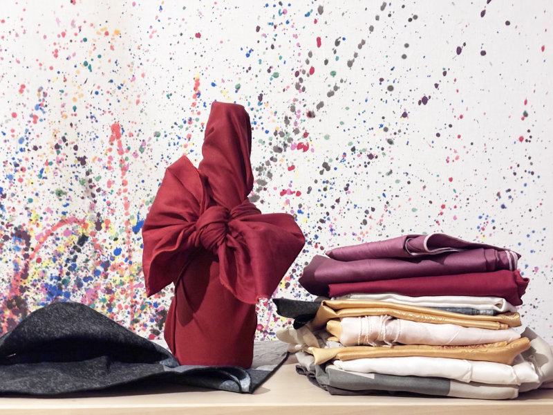 Eine mit einem Furoshikituch verpackte Flasche, daneben liegen noch gestapelt weitere Furoshiki Tücher